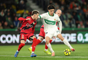 ELCHE, SPAIN - DECEMBER 21: Hector Fort of Elche CF is challenged by Isi Palazon and Pep Chavarria of Rayo Vallecano before breaking to score the team's first goal during the LaLiga EA Sports match between Elche CF and Rayo Vallecano de Madrid at Estadio Manuel Martinez Valero on December 21, 2025 in Elche, Spain. (Photo by Clive Brunskill/Getty Images)